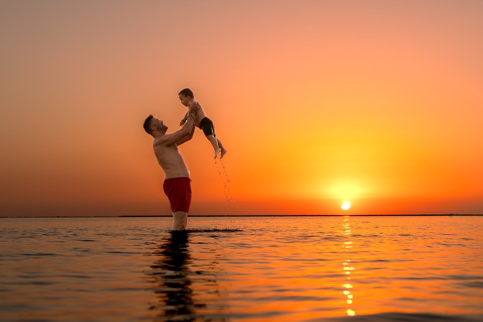 Padre levantando a su hija en el agua al atardecer